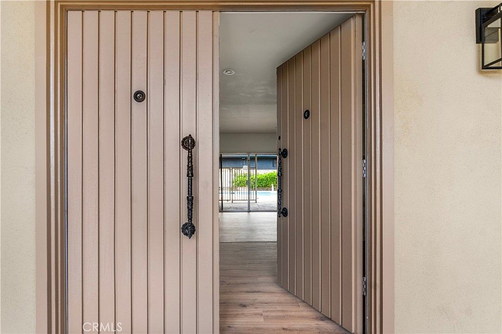 Looking through the open double front doors into the foyer, with hardwood flooring leading toward the rear sliding doors and the pool beyond