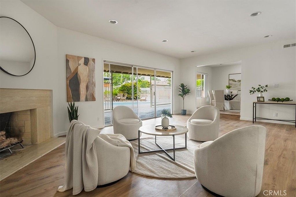 Living room with stone fireplace, large mirror over the mantel, hardwood flooring, swivel chairs around a low round table, and a wall of sliding glass doors opening to the covered patio and pool