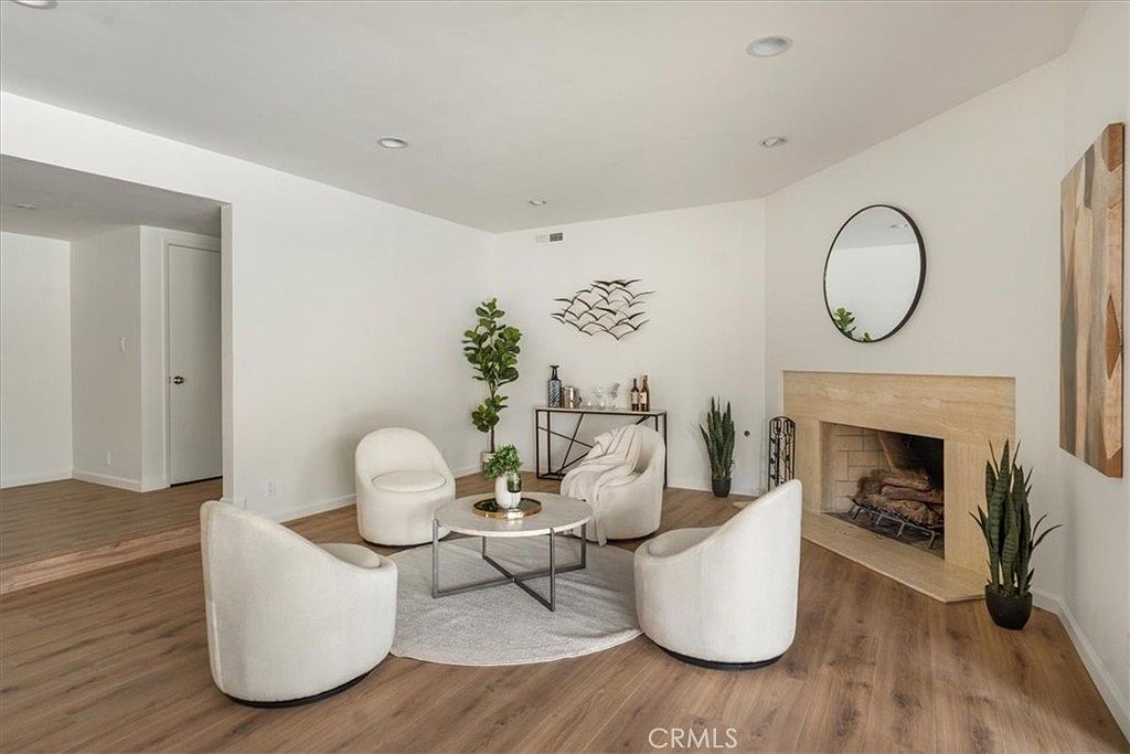 Second living area featuring a working stone fireplace with crackling logs, light wood mantel, abstract wood-toned art, and modern swivel chairs on a round area rug