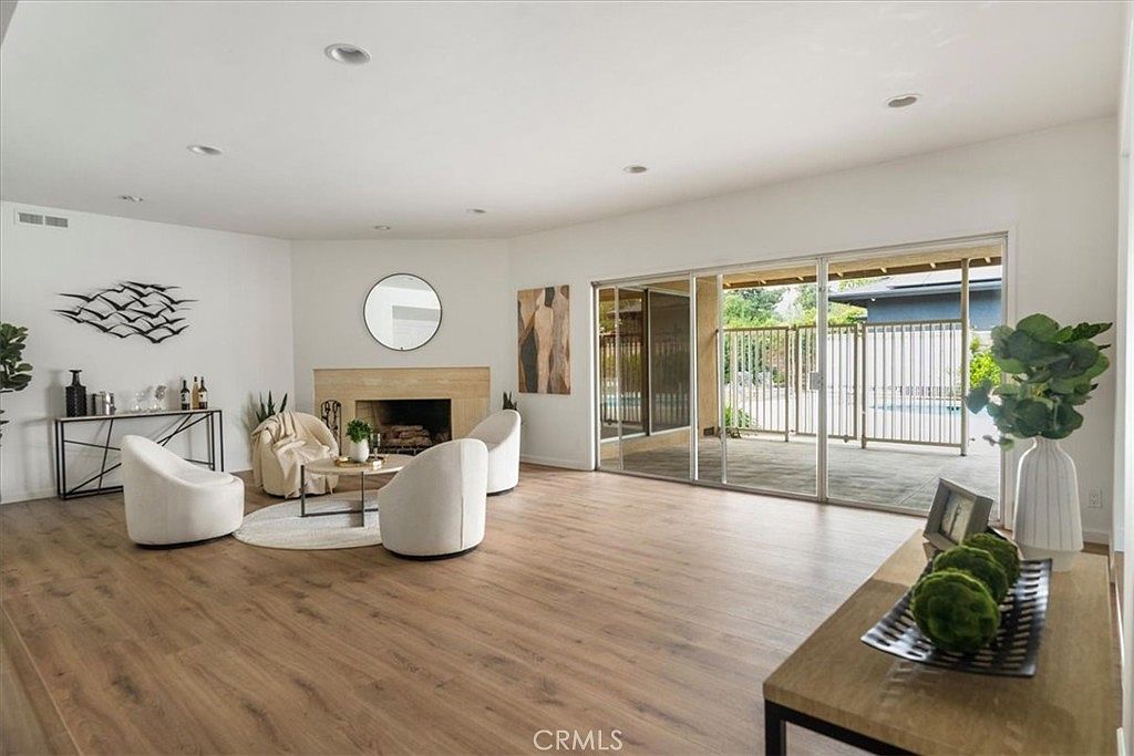 Open-concept great room with high ceilings, hardwood-style flooring, large mirror, layered seating around a round center table, and floor-to-ceiling sliding doors framing the gated pool yard